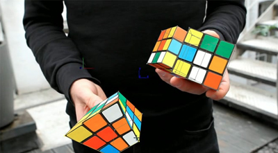 A person in a black long-sleeve shirt holding two colorful, digital 3D Rubik's cube models.