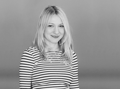 A blonde woman wearing a horizontal striped shirt smiles against a plain background.