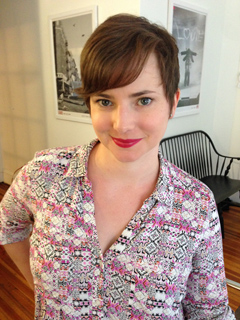 A woman with short brown hair and a pink patterned shirt smiles at the camera in an indoor setting.