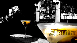 A gloved hand pours liquid into a martini glass in front of a blurred bar background.