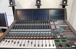 A large professional audio mixing console with multiple faders, knobs, and digital displays.