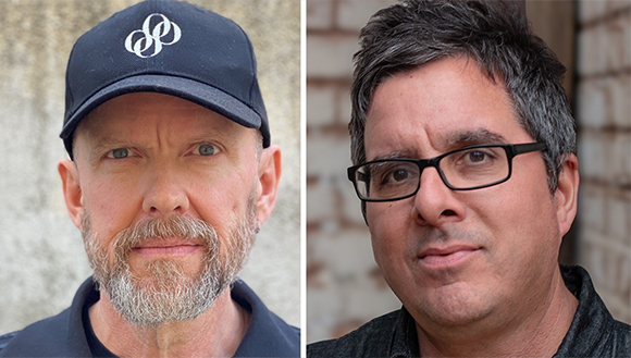 Two men looking at the camera, one wearing a black baseball cap and the other wearing black-rimmed glasses.