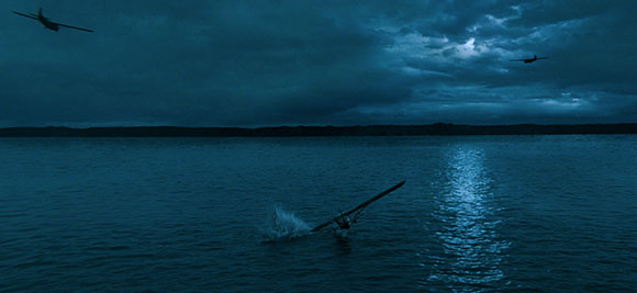 Two planes fly through a dark, cloudy sky over a vast ocean at dusk.