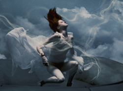 A woman with red hair in white flowing fabric poses against a cloudy, ethereal blue sky.