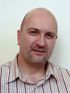 A bald man with light stubble wearing a brown and white striped collared shirt.