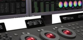 A color grading control panel with red trackballs in front of digital monitors displaying color correction tools.