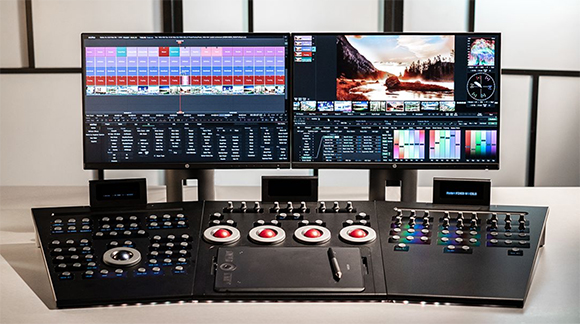Two computer monitors displaying video editing software above a large, multi-panel color grading control surface.
