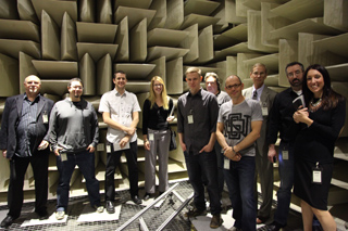 A group of nine people stand in an anechoic chamber with sound-dampening walls.