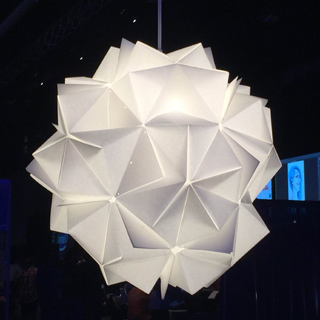 A white, geometric pendant light fixture made of folded paper panels, resembling an origami starburst.