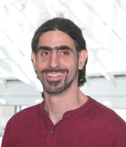 A man with dark hair and a goatee smiling in a maroon shirt.