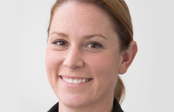 A smiling woman with light brown hair and freckles looking toward the camera against a white background.