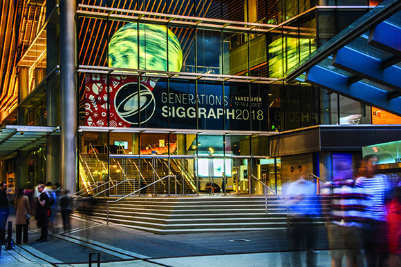 A glass building at night with a large SIGGRAPH 2018 banner and blurred people walking by.
