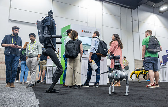 People standing around a large black humanoid robot and a small white quadruped robot at a tech booth.