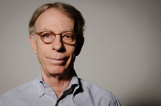 A man with short brown hair and glasses wearing a light blue striped button-down shirt.