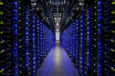 A long aisle in a data center lined with tall server racks glowing with blue and yellow lights.