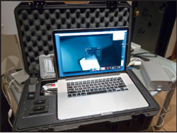 A silver laptop sits open inside a black protective carrying case lined with foam.