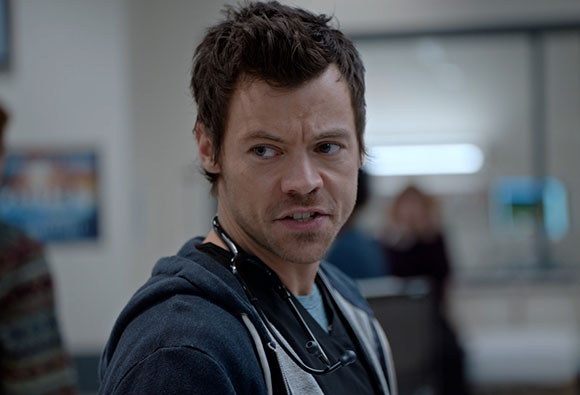 A man wearing a stethoscope and a dark hoodie looks to the side with a tense facial expression.