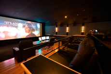 A dark screening room featuring a large movie screen, rows of leather seating, and a control desk.