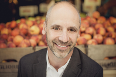A smiling man with short hair and a beard wearing a dark blazer and white shirt.