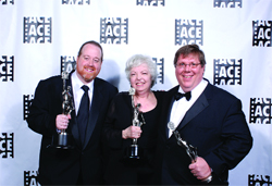 Three smiling people in formal attire holding silver trophies against a white backdrop with ACE logos.