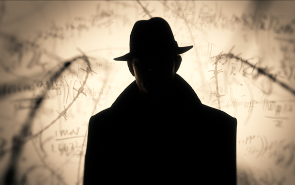 Silhouette of a person wearing a fedora and coat in front of a wall covered in mathematical formulas.