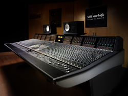 A large professional audio mixing console with numerous sliders and knobs in a dark studio setting.