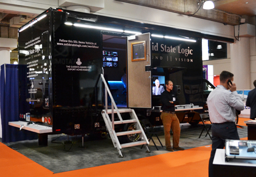 A black Solid State Logic mobile demo vehicle with stairs and a man standing nearby at an indoor event.