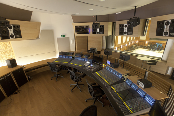 A wide view of a professional recording studio control room featuring a large mixing console and studio monitors.