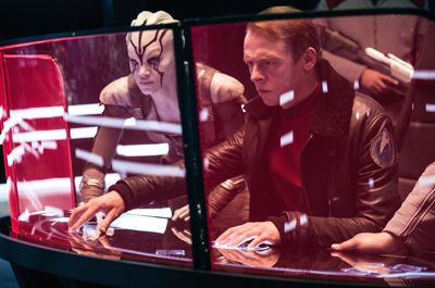 A man and a pale, patterned alien lean over a glowing red and white digital interface.