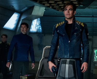 Three men in blue military-style uniforms stand on a futuristic spaceship bridge.