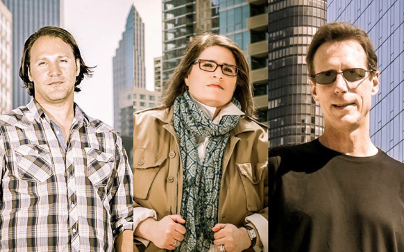 Three people posed in front of tall urban skyscrapers.