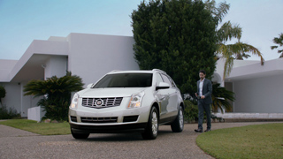 A white Cadillac SUV parked on a driveway in front of a large, modern white building with palm trees.