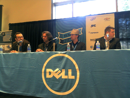 Four men sit at a long table with a large Dell logo during a panel discussion.