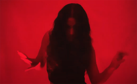 A dark silhouette of a person with long hair moving against a bright red background.