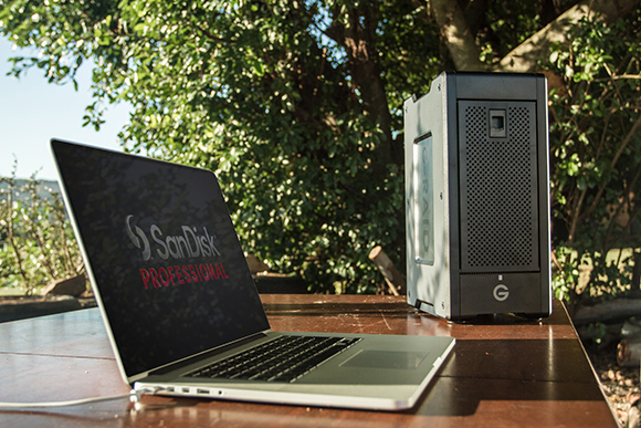 A laptop displaying the SanDisk Professional logo next to a black external hard drive on a wooden table.