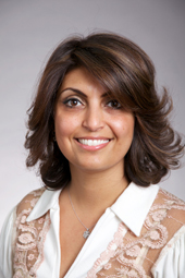 A woman with dark, layered hair and a white collared shirt with lace detailing smiles at the camera.