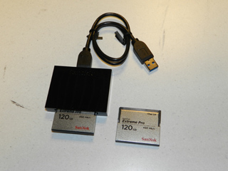 Black USB card reader connected to a cable, with two SanDisk Extreme Pro 120GB memory cards, one inserted into the reader and
