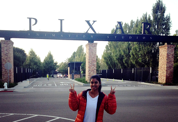 A woman in a red jacket makes peace signs in front of the Pixar Animation Studios gate.