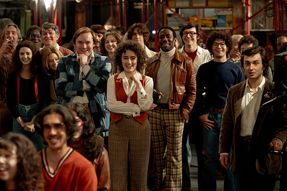 A diverse group of young adults smiling and posing closely together in a dimly lit room.
