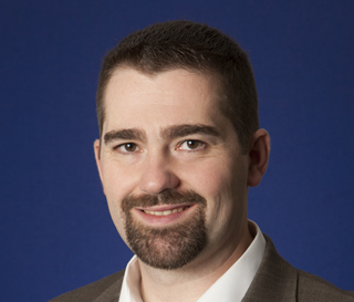 Man with short brown hair and a goatee smiling against a solid blue background