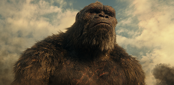 A large, brown-furred primate-like creature looks upward toward a cloudy sky.