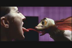 A person and a creature with large eyes touch their long tongues together.