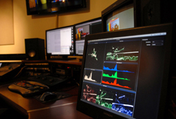 Several computer monitors in a dark studio showing video editing software and color waveforms.
