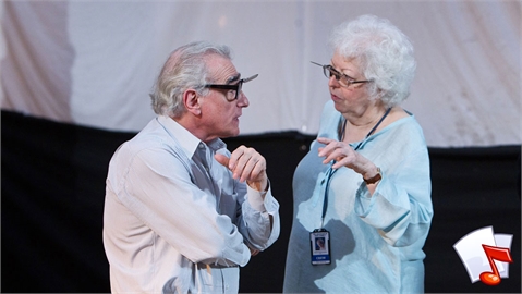 An older man in a white shirt talks to an older woman in a light blue shirt.