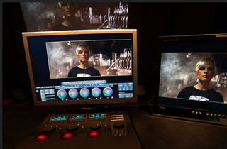 Two monitors showing video editing software with a woman's face on screen and a control panel in the foreground.