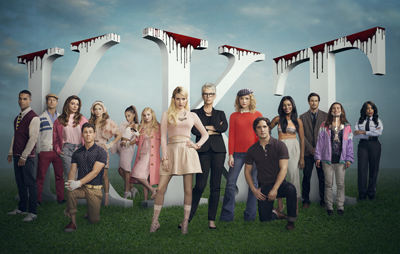 A group of young adults posing in front of large white letters dripping with red liquid.