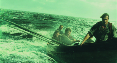 Four men struggle in a small wooden boat amidst turbulent, dark green ocean waves.