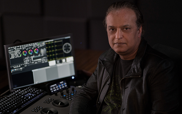A man in a black leather jacket sits before a computer monitor displaying video editing software.