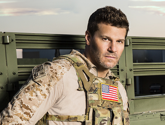 A man in desert camouflage tactical gear and a vest looking toward the camera.