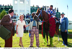 A group of people standing next to a brown horse decorated with red flowers on a grassy field.